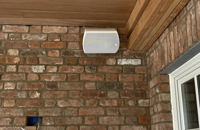 Outdoor speaker mounted under a wood porch ceiling on brick